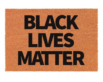 Może przedstawiać: Brązowa wycieraczka z napisem "BLACK LIVES MATTER" czarnymi literami.