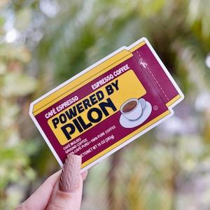 May include: A yellow and red sticker with the text "Café Espresso Espresso Coffee Powered by Pilon" and a small illustration of a cup of coffee. The text below the main text reads "Café Molido Ground Coffee 100% Café Puro 100% Pure Coffee Neto/Net Wt 10 oz (283g)".