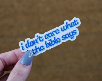 May include: A white sticker with blue text that reads "i don't care what the bible says". The text is in a retro font style.