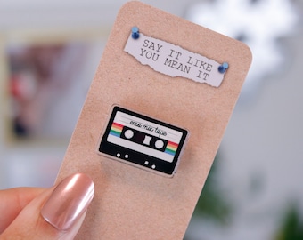 May include: A brown card with the text "Say it like you mean it" and a small, rainbow-colored cassette tape pin with the text "emo mix tape".