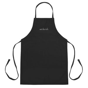 May include: Black apron with a large pocket and adjustable straps. The apron has the text "eat the rich." embroidered on the front.