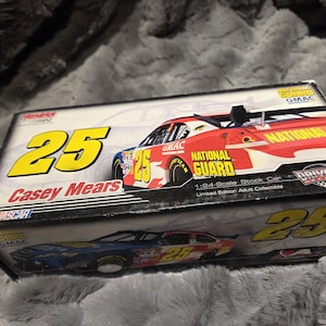 Könnte beinhalten: Ein verpacktes Casey Mears #25 National Guard Stock Car im Maßstab 1:24. Die Box zeigt das Auto in Rot, Weiß und Blau, mit der Nummer 25 in Gelb. Die Box zeigt auch den Text "Drivers Select" und "GMAC".