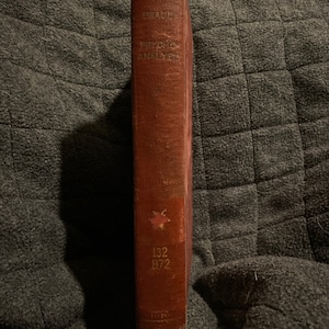 May include: A vintage, hardcover book with a worn, reddish-brown cover. The spine features the title "GRACE" and "PSYCHIC DISCOVERIES" in gold lettering. A small emblem and the numbers "132 B72" are also visible.