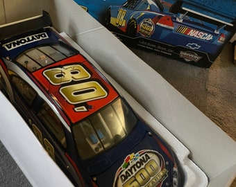 May include: A blue, red, and gold die-cast model car of a NASCAR race car. The car is in a white box with the Daytona 500 logo and the text "50 Years The Great American Race 2008". The car has the number "08" on it.