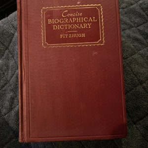 Peut inclure: Un livre marron intitulé "Concise Biographical Dictionary" avec des lettres dorées et une bordure décorative. Le nom de l'auteur, Fitzhugh, est également en or. Le livre a une couverture texturée.