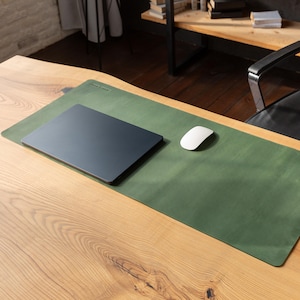 Könnte beinhalten: Eine grüne Schreibtischunterlage aus Leder mit einem dunkelgrauen Laptop und einer weißen Computermaus. Die Schreibtischunterlage ist rechteckig und liegt auf einem Holztisch. Der Laptop ist geschlossen.