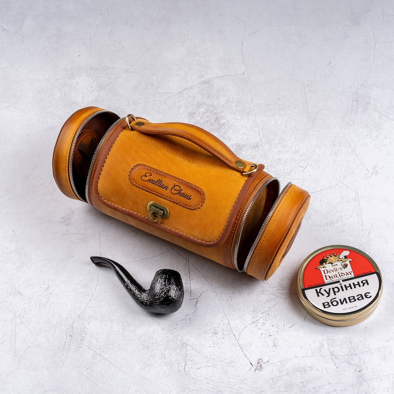 May include: A brown leather travel case with a zippered opening and a handle. The case has the words "Exelllan Chaus" embossed on the front. A black pipe and a round tin of "Devil's Holiday" tobacco are also pictured.