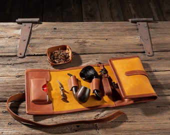 May include: A brown leather pipe carrying case with a yellow suede lining. The case has a pocket for a lighter and a small pouch for tobacco. The case is open and shows two pipes, a tamper, and a pouch of tobacco.
