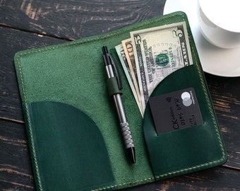 May include: A green leather wallet with a pen, cash, and a credit card inside. The wallet has a flap that closes with a snap.