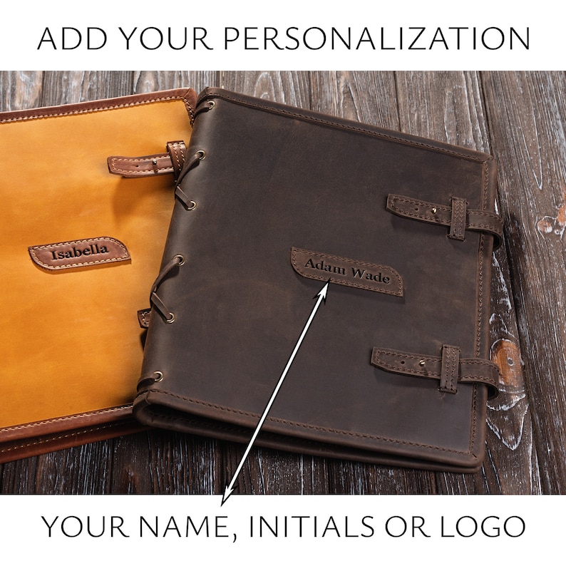 May include: Two brown leather journals with a lace-up closure. One journal has the name "Isabella" embossed on it, and the other has the name "Adam Wade" embossed on it.  The journals are on a wooden surface.