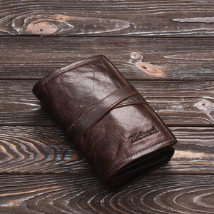 May include: A brown leather wallet with a fold-over closure and a stitched strap. The wallet has the word "Richard" embossed on the front.