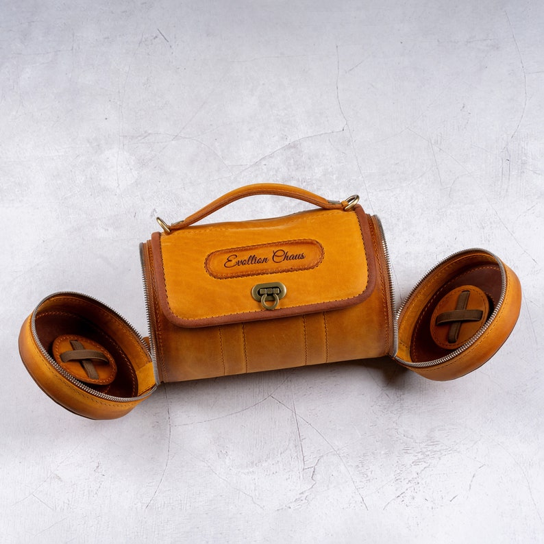May include: A brown leather cylindrical bag with a top handle and a metal clasp. The bag has a personalized inscription that reads "Evellion Chaus".