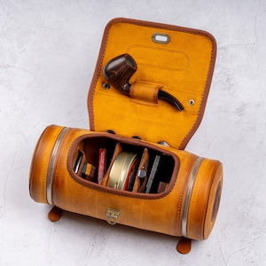 May include: A brown leather travel case with a zippered closure and multiple compartments. The case is open and reveals a pipe, a small jar, and other accessories.