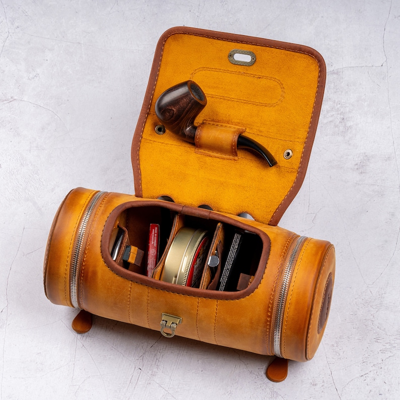 May include: A brown leather travel case with a zippered closure and multiple compartments. The case is open and reveals a pipe, a small jar, and other accessories.