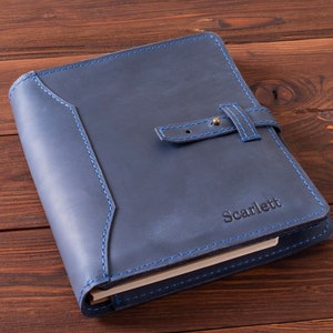 May include: A navy blue leather journal with a blue stitching detail and a brass buckle closure. The journal is personalized with the name "Scarlett" in gold lettering.