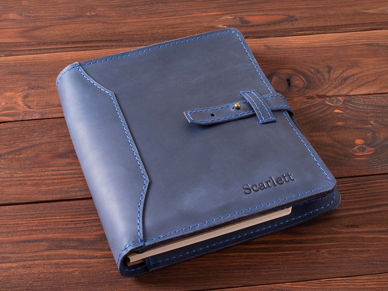 May include: A navy blue leather journal with a blue stitching detail and a brass buckle closure. The journal is personalized with the name "Scarlett" in gold lettering.