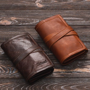 May include: Two leather wallets, one brown and one dark brown, with a strap closure. The wallets are on a wooden surface.