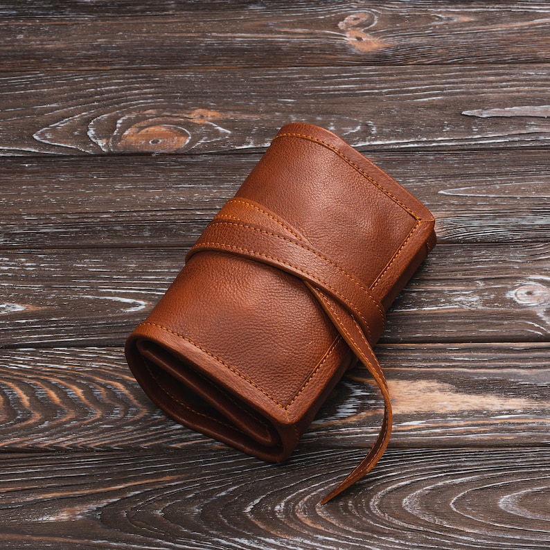 May include: A brown leather roll-up case with a strap closure. The case is rolled up and tied with the strap.