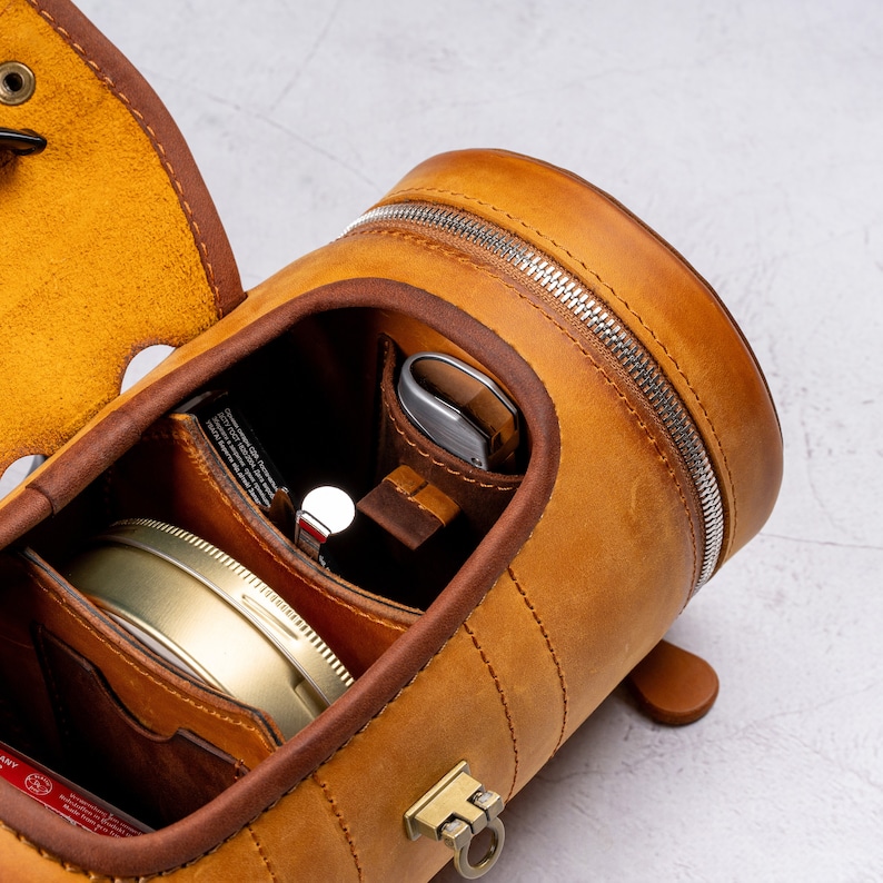 May include: A brown leather travel case with a zipper closure and multiple compartments. The case is open to reveal a small round container, a metal tool, and a brown leather pouch.