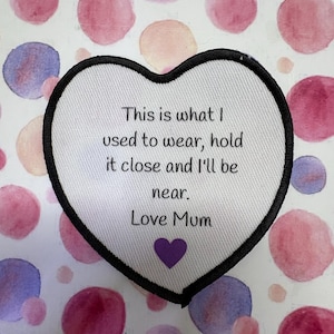 May include: A heart-shaped patch with a black border and white fabric. The patch has the text "This is what I used to wear, hold it close and I'll be near. Love Mum" and a purple heart.