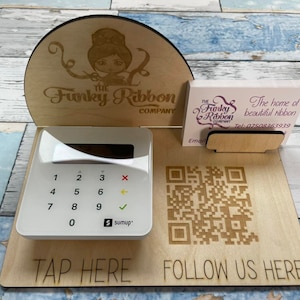 May include: A wooden stand with a logo for "The Funky Ribbon Company" featuring a cartoon woman with a ribbon. The stand has a card holder, a card reader, and a QR code with the text "Follow Us Here".