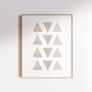 May include: A framed print with a minimalist design featuring a vertical row of 10 beige watercolour triangles. The print has a light brown wood frame. The text "Buy 2 (or more) prints & get 1 FREE!" is at the bottom of the image.