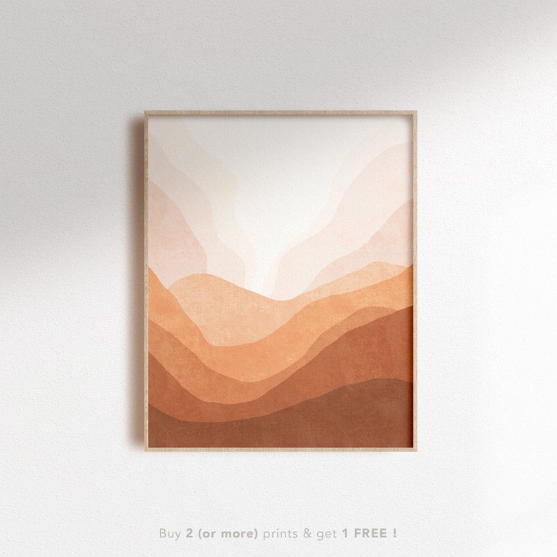 May include: Abstract art print featuring a landscape of layered, watercolor-like hills in shades of orange, brown, and pink. The print is framed in a light wood frame.