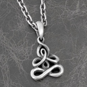 Puede incluir: Un collar de cadena de plata con un colgante de plata en forma de nudo estilizado. El colgante es un diseño complejo con múltiples bucles y curvas.