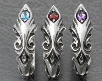 May include: Three silver-toned rings with ornate, swirling designs. Each ring features a gemstone: one blue, one red, and one purple. The rings are displayed on a gray surface, showcasing their intricate details and varied colors.