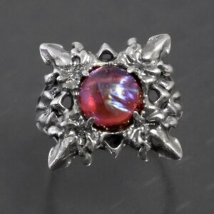 May include: A silver ring with a red and iridescent gemstone set in a detailed, intricate design.