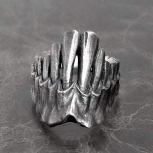 May include: A silver ring with a detailed design of a set of teeth. The ring is made to look like a jawbone.