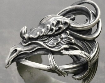 May include: A silver ring with a detailed design of a bird's head with intricate feathers and a swirling pattern.