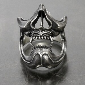 May include: A silver ring with a detailed skull design. The skull has a wide open mouth with sharp teeth and a prominent nose.
