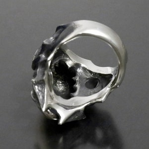 May include: A silver ring with a detailed, textured design. The ring is open on the back, revealing a hollow interior.