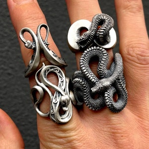Op de afbeelding: Drie zilveren ringen met slangendesigns. De ringen worden gedragen aan de vingers van een persoon.