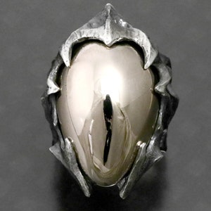 May include: A silver ring with a large, smooth, oval-shaped gemstone set in a detailed, textured, and intricate design.
