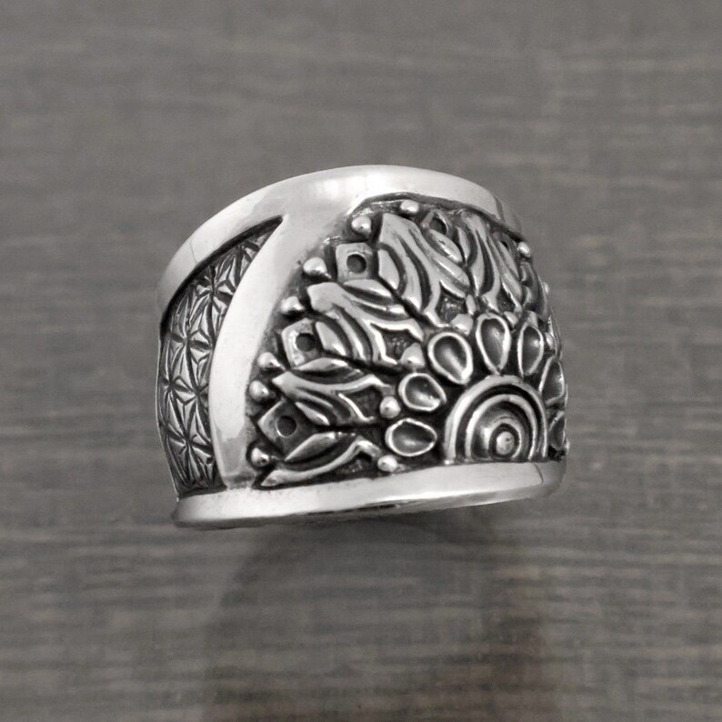 May include: A silver ring with a detailed mandala design. The ring is wide and has a rounded top.