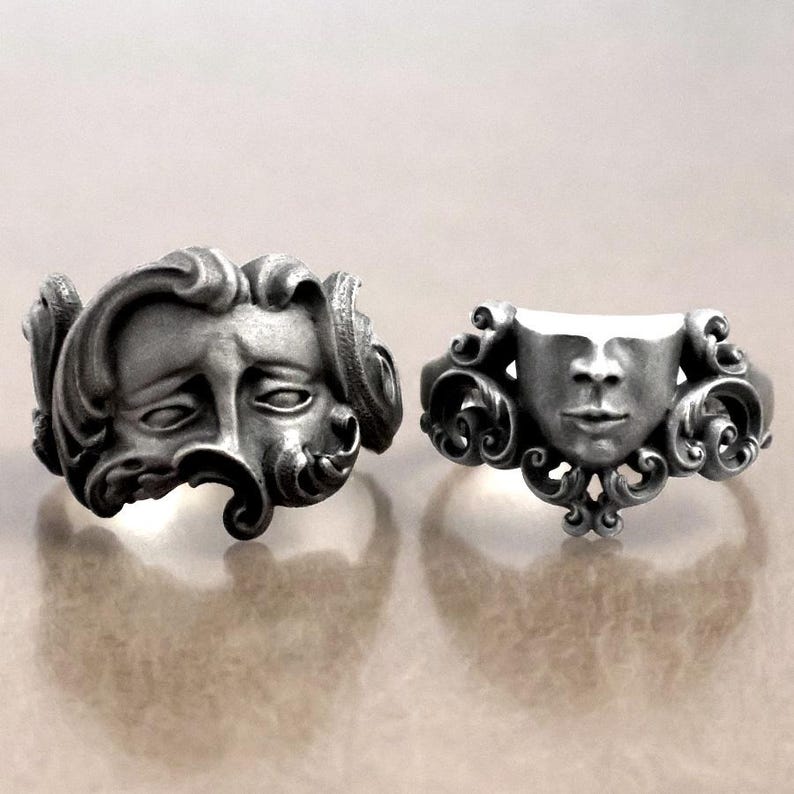 K&ouml;nnte beinhalten: Zwei silberfarbene Ringe mit detaillierten Gesichtsdesigns. Ein Ring zeigt ein volles Gesicht mit flie&szlig;endem Haar, der andere ein teilweises Gesichtsdesign. Beide Ringe haben aufwendige, verzierte Details und zeigen eine gotische oder Vintage-&Auml;sthetik.