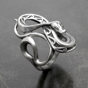 Op de afbeelding: Een zilveren slangenring met ingewikkelde details. De slang is opgerold en zijn kop is opgeheven, met een klein oogdetail. De ring is gemaakt van glad, gepolijst metaal.