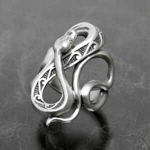 Op de afbeelding: Een zilveren ring met een gedetailleerd slangendesign. De slang is opgerold en ingewikkeld gesculpteerd met een textuur.