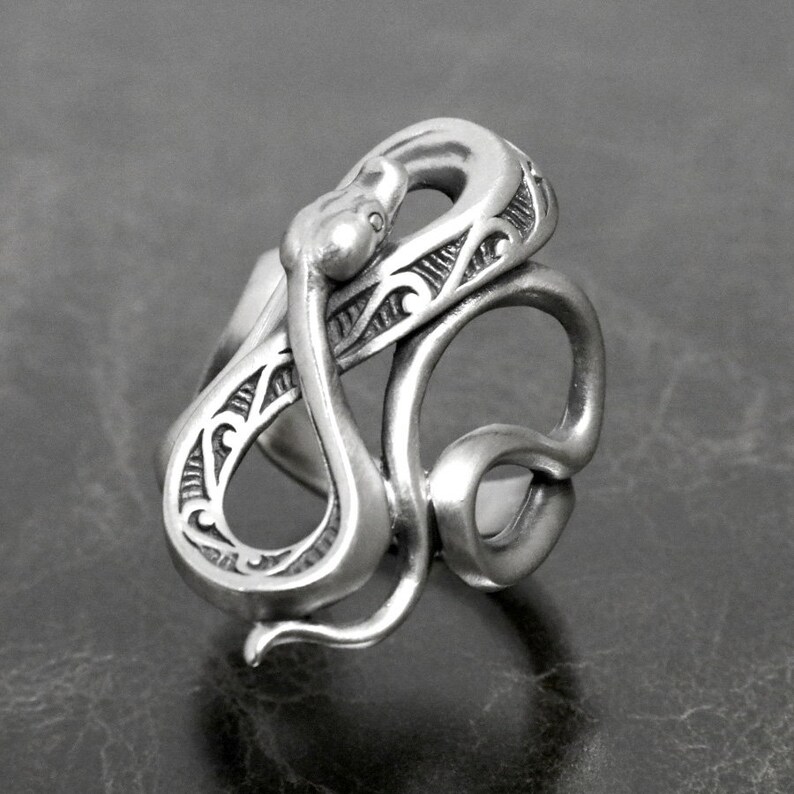 Op de afbeelding: Een zilveren ring met een gedetailleerd slangendesign. De slang is opgerold en ingewikkeld gesculpteerd met een textuur.