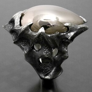 May include: A silver ring with a large, round, gold-colored stone set in a textured, organic-shaped setting.