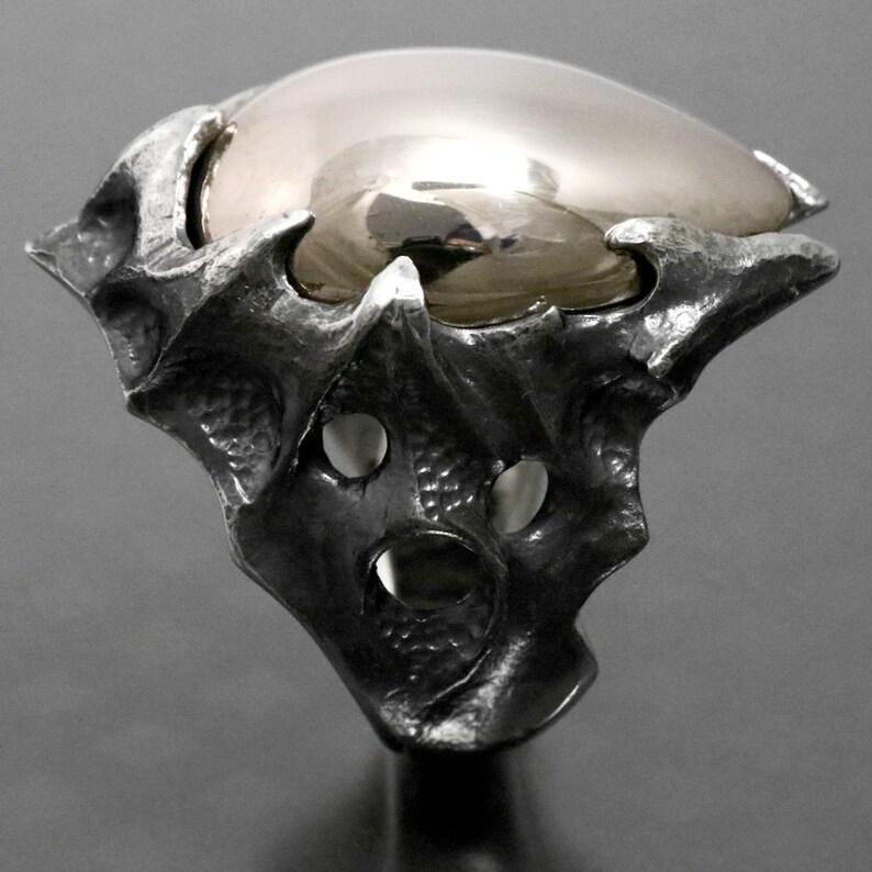 May include: A silver ring with a large, round, gold-colored stone set in a textured, organic-shaped setting.