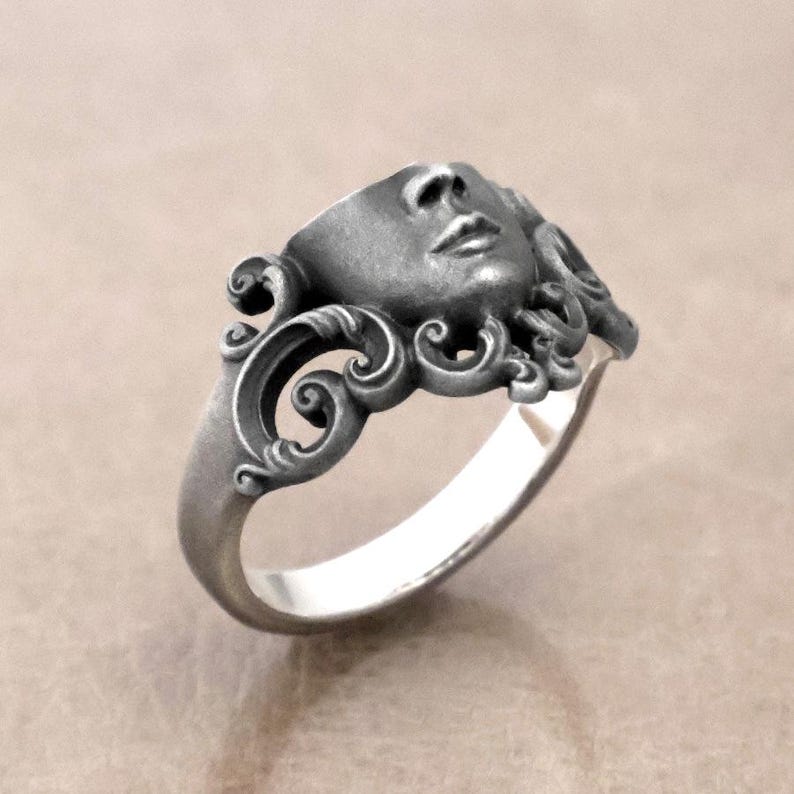 K&ouml;nnte beinhalten: Silberner Ring mit einer modellierten Gesichtsform, detaillierten Gesichtsz&uuml;gen und flie&szlig;endem Haar. Der Ring hat ein verziertes, wirbelndes Design um das Gesicht und einen glatten, polierten Ring. Ein einzigartiges Schmuckst&uuml;ck.