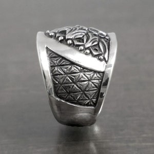 May include: A silver ring with intricate floral designs on the top and a geometric pattern on the band.