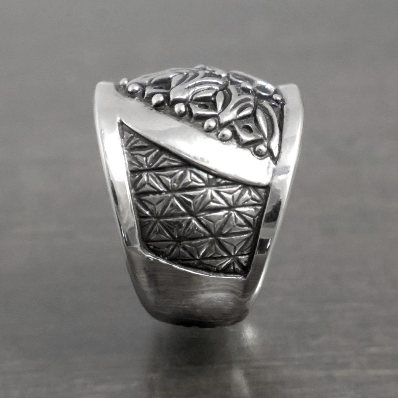 May include: A silver ring with intricate floral designs on the top and a geometric pattern on the band.