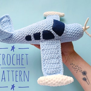 May include: A crocheted airplane toy in light blue with white accents. The airplane has a blue and white propeller and a dark blue window. The text "CROCHET PATTERN" is written in blue on a white background.