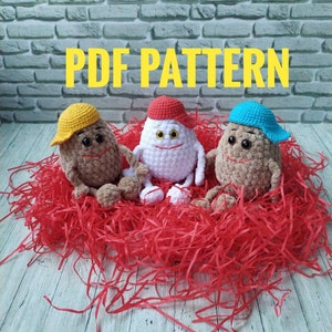 Könnte beinhalten: Drei gehäkelte Amigurumi-Spielzeuge, zwei braune und ein weißes, mit lächelnden Gesichtern und Hüten. Die braunen Spielzeuge haben gelbe und blaue Hüte, während das weiße Spielzeug einen roten Hut hat. Die Spielzeuge sitzen auf einem Bett aus rotem zerkleinertem Papier.