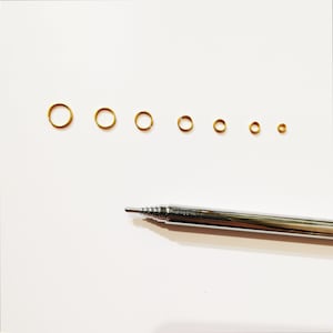 May include: A set of eight gold jump rings of varying sizes, arranged in order from largest to smallest. A silver retractable pen is also pictured.