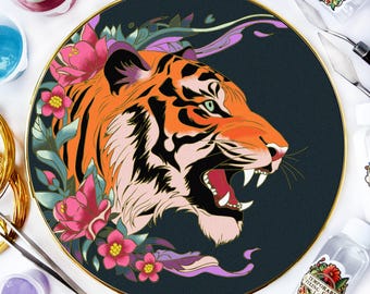 May include: A circular embroidery hoop featuring a detailed illustration of a tiger head in profile with its mouth open, surrounded by pink flowers and green leaves on a dark background, accompanied by art supplies and a bottle labeled ERSENN.